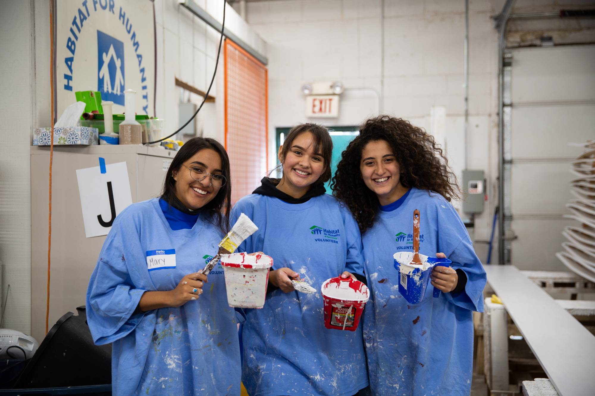 Students wearing smocks and holding paint brushes, smiling at the camera